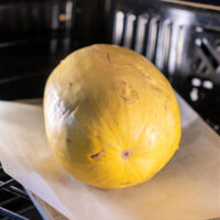 A whole yellow spaghetti squash is roasting to perfection on parchment paper, nestled in the warmth of the oven.