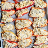 Stuffed mini sweet peppers are halved and laid out on a baking sheet, topped with a delightful mixture of cheese and herbs. These vibrant treats are carefully arranged in rows on parchment paper.