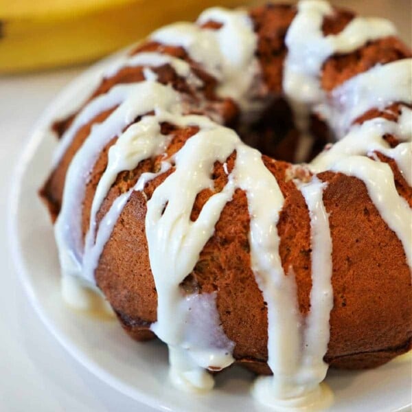 A glazed bundt cake sits enticingly on a white plate, with a banana in the background, hinting at a perfect air fryer breakfast treat.