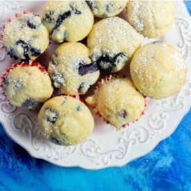 A plate of blueberry pancake mix muffins dusted with powdered sugar on a blue background.