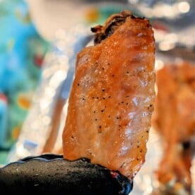 A baked turkey wing is held by black tongs above a foil-covered surface. The wing appears seasoned and crispy.