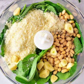 Combine all the fresh ingredients for pesto with pine nuts in a food processor, including vibrant spinach, aromatic garlic, and rich cheese.