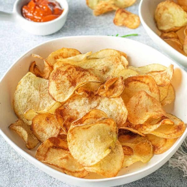 A bowl of crispy russet potato chips sits elegantly with a small dish of ketchup in the background, inviting a delightful snacking experience.