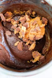 A thick chocolate fudge batter in a bowl is enhanced with chopped peanut butter cups and a dollop of creamy peanut butter, reminiscent of a rich fudge infused with the sweetness of condensed milk.