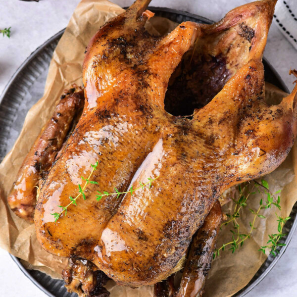 Roast Duck Recipe: Savor the exquisite taste of roasted duck, elegantly garnished with thyme on a round plate lined with parchment paper, accompanied by a bowl of cherry tomatoes.