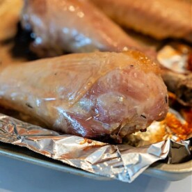 Close-up of a baked turkey leg resting on a piece of aluminum foil on a baking tray. The golden-brown exterior showcases the perfectly roasted appeal of baked turkey legs.