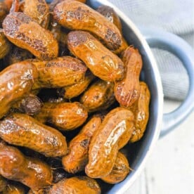 A bowl of Crockpot boiled peanuts sits on a wooden surface, complemented by a gray cloth in the background.