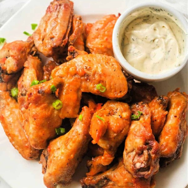 A plate of hot wings cooked to perfection in the air fryer is garnished with green onions and served alongside a small bowl of creamy dipping sauce.