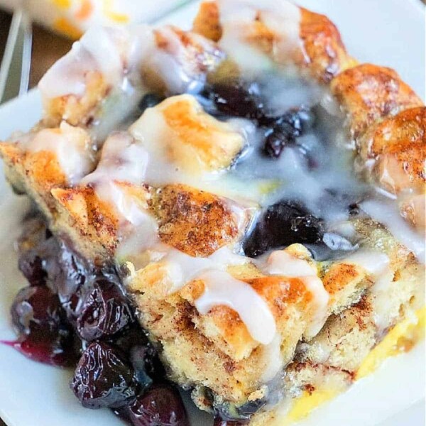 A glazed blueberry pastry on a white plate, with layers of bread and visible cherry filling, evokes the comforting warmth of a cinnamon roll—a delightful breakfast casserole treat.