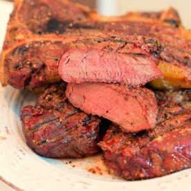 A plate featuring several slices of smoked steak at 250 degrees, showcasing a perfect sear on the outside with a tender, pink interior. The seasoned steak is artfully arranged on a pristine white plate.