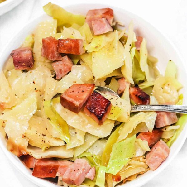 A bowl of cabbage and diced ham, perfectly seasoned and served with a fork.