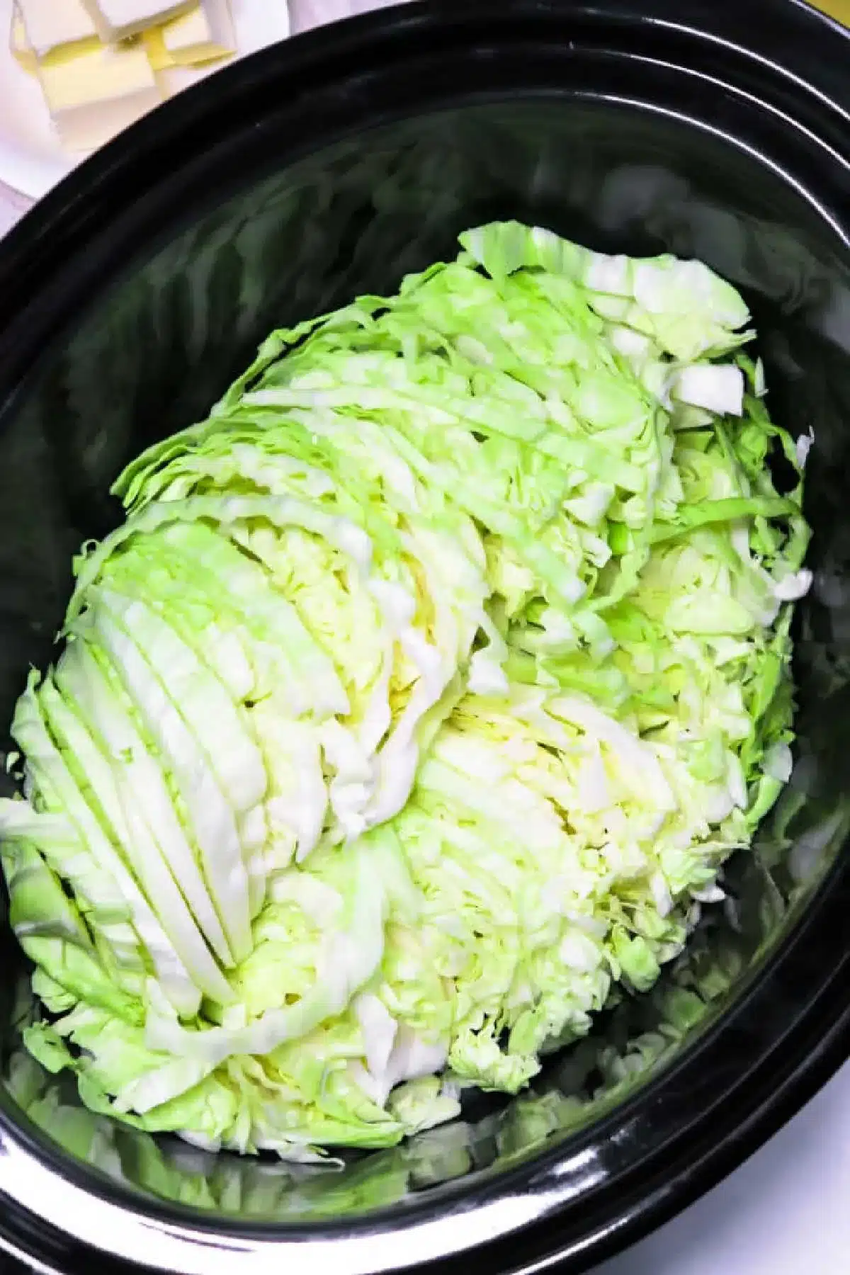 A heap of slow cooker cabbage rests inside a sleek black cooker, primed for a delicious transformation.