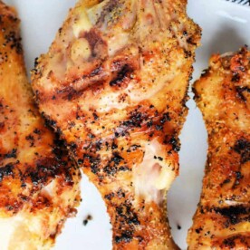 Close-up of grilled, seasoned chicken drumsticks on a white plate.