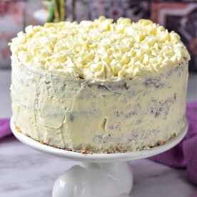 A white frosted cake on a rabbit-shaped stand, topped with white chocolate curls, sits enticingly in front of a patterned background, seemingly asking: "How long does it take to bake perfection?