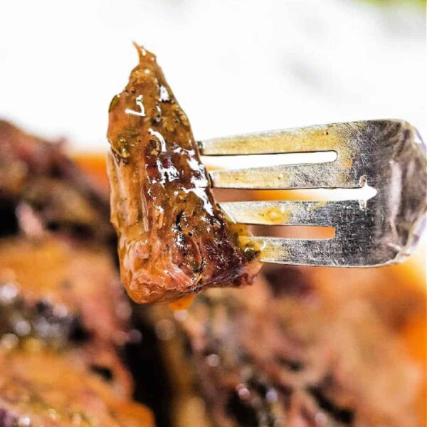 A close-up of a fork holding a juicy piece of glazed meat, cooked to perfection, with more fall-apart sirloin tip roast blurred in the background.