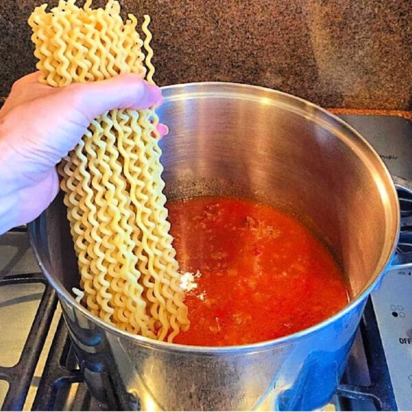 A hand gracefully holds uncooked pasta over a simmering pot of red sauce on the stove, capturing the essence of one-pot spaghetti perfection.