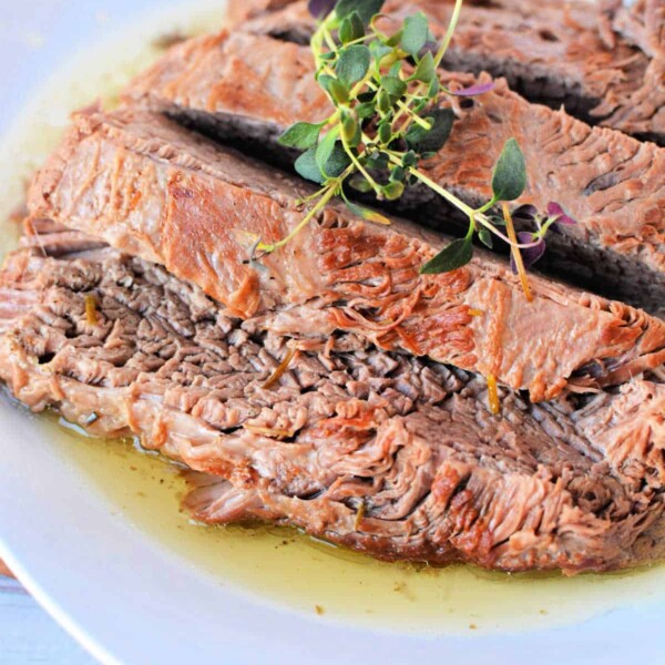 Sliced pressure cooker brisket with gravy on a white plate, garnished with fresh herbs.