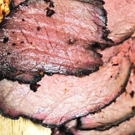 A close-up of several slices of succulent Sirloin Tip Roast, with a browned crust and pink interior, elegantly arranged on a wooden cutting board.