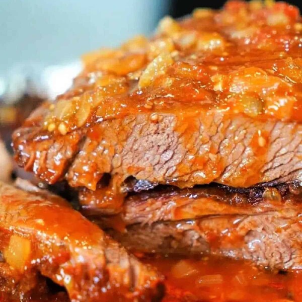 Close-up of savory brisket, slow-cooked in the oven, topped with a rich, chunky tomato sauce.