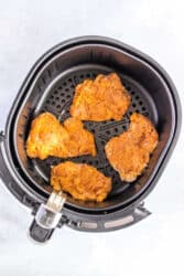 Four seasoned chicken thighs sit invitingly in an air fryer basket, their crispy edges reminiscent of perfectly cooked fried chicken thighs.