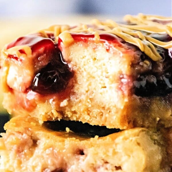 Close-up of a decadent Peanut Butter and Jelly Cheesecake Bar with a bite taken out, revealing its luscious layers of filling and topping.