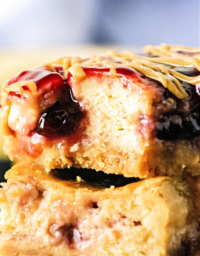 Close-up of a decadent Peanut Butter and Jelly Cheesecake Bar with a bite taken out, revealing its luscious layers of filling and topping.