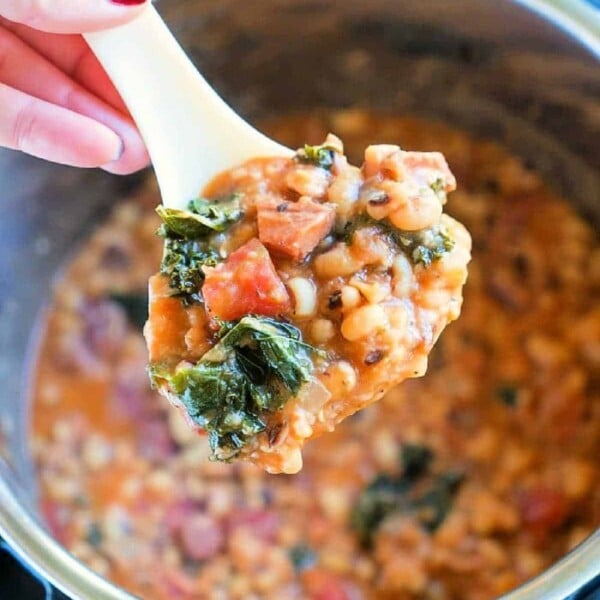 A spoonful of hearty stew with beans, greens, and sausage over a pot delivers the comforting essence of slow cooker hoppin’ john.