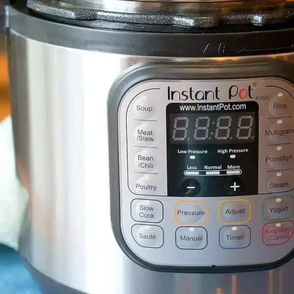 The Instant Pot's sleek digital display, currently turned off, invites exploration of its versatile settings for soup, meat/stew, and beans/chili. Resting on a blue surface with a touch of green cloth beside it, this image sparks curiosity about how to use an Instant Pot effectively.