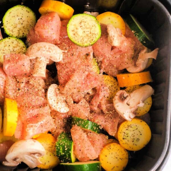 Air fryer chicken and vegetables come to life with chopped chicken, zucchini, yellow squash, and mushrooms seasoned to perfection in an air fryer basket.