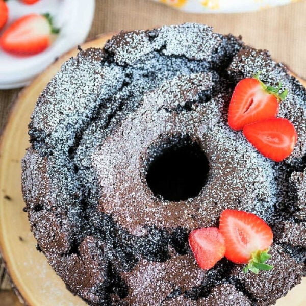 Chocolate bundt cake made with a twist from an angel food cake mix recipe, topped with a dusting of powdered sugar and slices of fresh strawberries.
