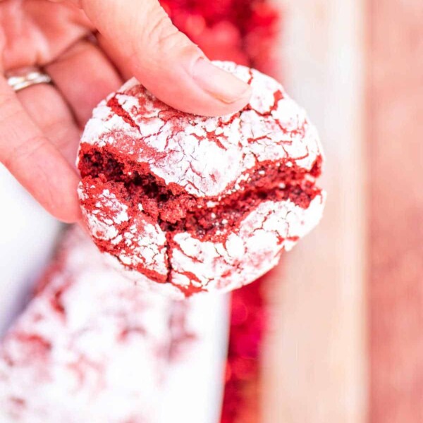 A hand holding a cracked cake mix red velvet crinkle cookie, dusted with powdered sugar.