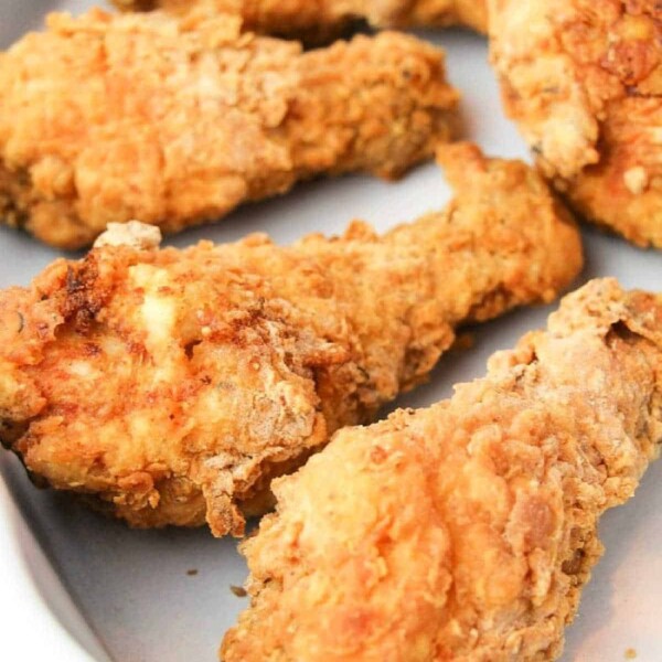 Four pieces of crispy fried chicken on a white plate, capturing the essence of a copycat Kentucky Fried Chicken recipe.