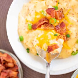 A bowl of Hashbrown Soup on Stove topped with cheese, bacon, and green onions sits invitingly beside a steaming pot of frozen Hashbrown Soup warming on the stove.