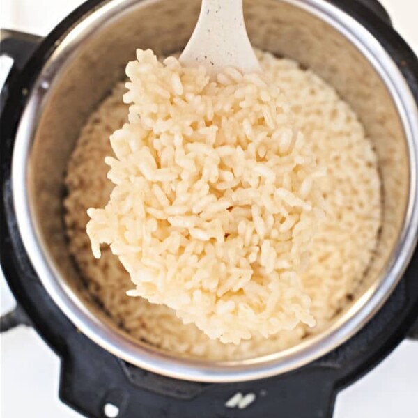 A white spatula lifts perfectly cooked Arborio rice from an electric pressure cooker, demonstrating how to achieve creamy perfection.