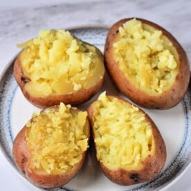 Four halved baked sweet potatoes with mashed insides sit on a plate, a tempting twist on comfort food that rivals even the most tender Instant Pot red potatoes.