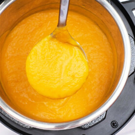 A ladle serves creamy kabocha squash soup from an Instant Pot, its rich orange hue inviting a comforting taste.