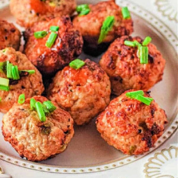 A white plate holds several browned air fryer chicken meatballs garnished with chopped green onions. The plate features an ornate border design.