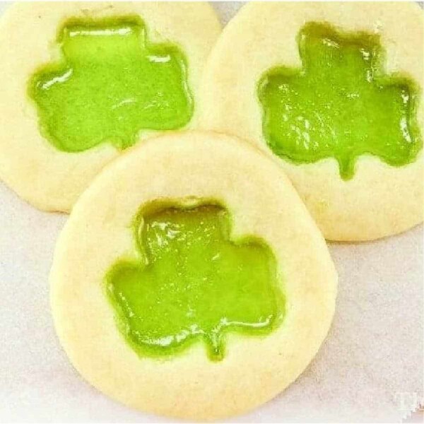 Discover how to make Stained Glass Cookies with a touch of charm—three cookies featuring vibrant green shamrock-shaped jelly centers beautifully displayed on a light background.