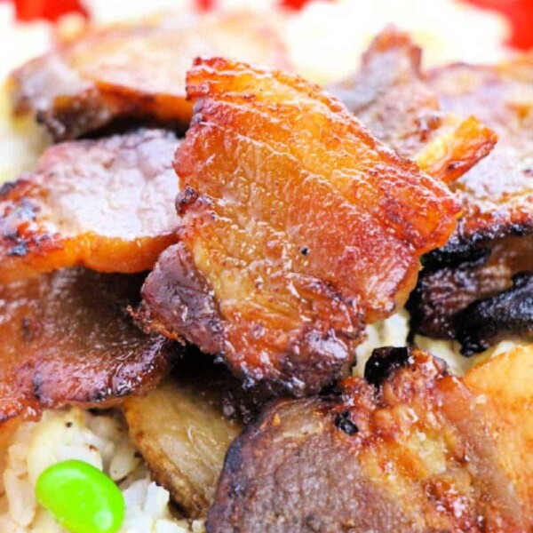 A close-up of crispy pork belly, oven-cooked to perfection, on rice with green peas, served on a vibrant red plate.