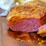 Close-up of a sliced corned beef brisket with a golden crust on a wooden cutting board, hinting at smoky Traeger flavors.