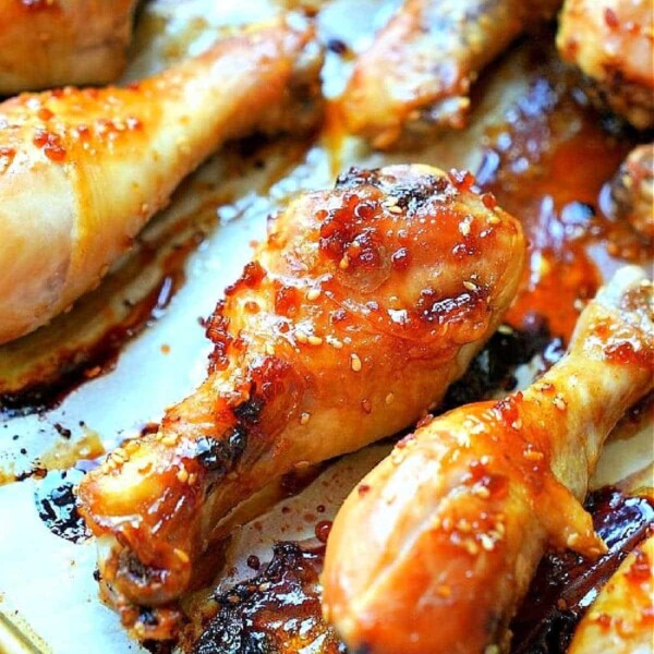 Close-up of roasted teriyaki chicken drumsticks, coated with a glossy, caramelized glaze and sprinkled with coarse salt. They rest on a parchment-lined baking sheet, showcasing their browned and crispy edges.