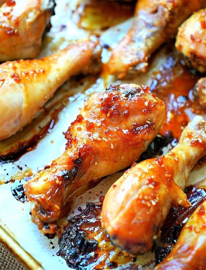 Close-up of roasted teriyaki chicken drumsticks, coated with a glossy, caramelized glaze and sprinkled with coarse salt. They rest on a parchment-lined baking sheet, showcasing their browned and crispy edges.