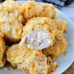 Plate of golden, crispy air fryer chicken nuggets with one piece showing juicy white meat inside.