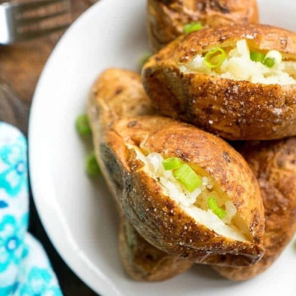 Baked potatoes on a plate, crowned with butter and chopped green onions, alongside a fork and napkin—perfect inspiration for your next potato recipe ideas.