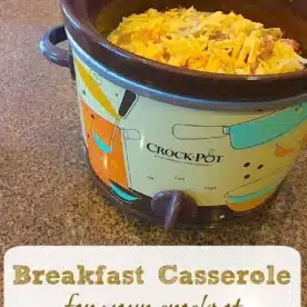 A Crock-Pot sits on a countertop filled with a mouthwatering crockpot breakfast casserole recipe, topped with shredded cheese. The text on the image reads, Breakfast Casserole for your crockpot.