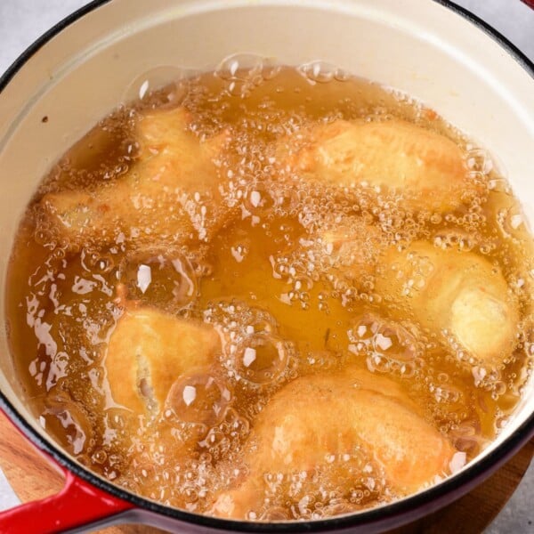 tempura chicken wings cook in hot oil inside a red pot placed on a wooden surface, much like the ambiance created when timing how long to deep fry chicken wings for that perfect crispy texture.