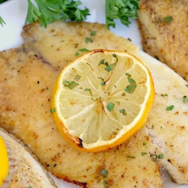 Seasoned frozen fish in air fryer fillet garnished with parsley and a slice of lemon, served on a white plate.