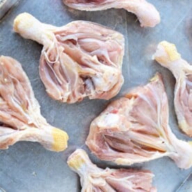 Butterflied chicken legs with skin partially removed are neatly arranged on a metal baking sheet.