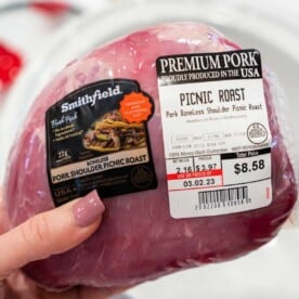 A hand holds a packaged Pork Picnic Roast, its label clearly displaying the price and weight.