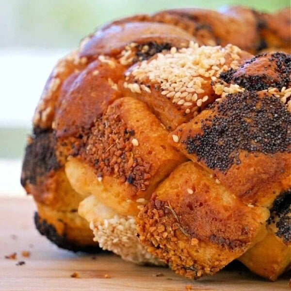 Close-up of a savory monkey bread loaf, elegantly braided and topped with sesame and poppy seeds, resting on a rustic wooden surface.